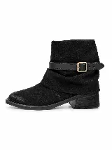 Bota corta de gamuza negra con diseño de caña holgada y correa decorativa con hebilla metálica. Presenta un taco cuadrado bajo y punta redondeada.