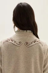 Sweater de tejido de punto color beige con diseño de arabescos en tonos marrones en hombros y mangas. Presenta cuello redondo con cordones decorativos y puños con textura acanalada.