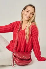 Bandolera de cuero vacuno color rojo, con diseño de solapa decorada con tachas metálicas plateadas. Cuenta con cierre central, correa regulable de cinta al tono y bolsillo trasero con cierre.