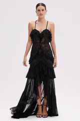 Vestido largo de tul negro con tirantes finos, escote en V con volantes, cuerpo ajustado con bordados y abalorios, y falda con volantes en capas y bajo asimétrico.