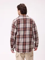 Camisa de franela gruesa con diseño a cuadros en tonos marrones, beige y azul. Presenta cuello clásico, cierre frontal con botones y dos bolsillos en el pecho con solapa y botón.