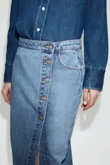 Falda midi de denim azul con diseño cruzado, cierre frontal con botones metálicos y bolsillos delanteros.