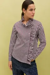 Camisa de algodón con estampado de rayas verticales en color bordó y blanco. Presenta un diseño de manga larga con puños abotonados, cuello camisero y un detalle de volado lateral que recorre el frente desde el cuello hasta el ruedo, acompañando la línea de botones.