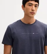 Remera de corte comfort, color azul melange, con cuello redondo, manga corta y estampa frontal localizada con texto pequeño.