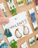 Caravanas de diseño minimalista con forma de gota, compuestas por un centro de resina nacarada en tono crema enmarcado en una estructura metálica dorada.