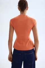 Top de tejido de punto fino color naranja, con cuello redondo acanalado, mangas cortas raglán y un ligero peplum en el bajo.