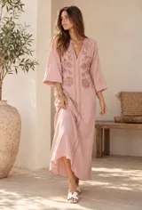 Vestido largo beige con escote en V y mangas largas abullonadas, adornado con delicados bordados florales en tono tostado en la parte frontal y cenefas decorativas a lo largo de la abertura central.