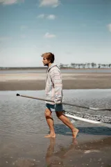 Buzo con capucha de tejido grueso a rayas horizontales en tonos pastel: celeste, rosa y gris. Tiene bolsillo tipo canguro y cordones ajustables en el cuello.