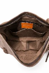 Cartera tipo hobo de cuero vacuno color tostado, con diseño amplio y flexible, decorada con un trenzado artesanal en el frente y largos flecos laterales. Cuenta con correa larga para llevar al hombro.