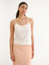 Blusa blanca sin mangas, confeccionada en tela ligera y fluida, con escote redondo y tirantes finos.