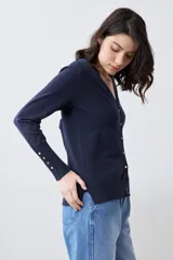 Cardigan de punto negro con escote en V, cierre frontal con botones metálicos dorados y mangas largas con puños ajustados que incluyen detalles de botones decorativos.
