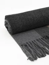 Bufanda tipo pashmina de tejido suave, color gris con diseño de cuadros en tonos oscuros y líneas finas en rosa. Presenta terminaciones con flecos en los extremos.
