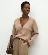 Cardigan de punto color beige con escote en V, cierre frontal con botones grandes y mangas largas con puños acanalados. Presenta un corte recto y estructurado.