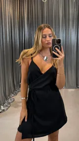 Vestido corto negro con breteles finos, escote cruzado y falda cruzada con lazo lateral.