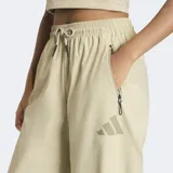 Pantalon Adidas Z.N.E. de corte holgado, confeccionado en tejido ripstop color beige. Presenta cintura elástica con cordón de ajuste, bolsillos laterales con cierre y detalles de estampado en caucho mate.