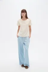 Blusa de viscosa color natural, con cuello a la base, manga corta y detalle de plisado cruzado en el frente. Presenta un corte holgado.