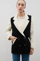 Blazer de lana con diseño bicolor, cuerpo en color negro y mangas en color crema. Presenta un corte holgado, cierre cruzado con doble botonadura y solapas amplias en contraste.