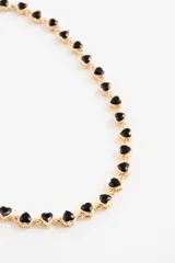 Collar tipo gargantilla con cadena dorada y dijes en forma de corazón de color negro.