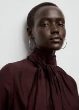 Blusa de cuello alto con detalle de fular integrado, confeccionada en tejido con textura. Presenta diseño recto, manga larga con puños abotonados y cierre posterior.