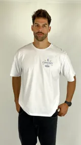 Remera de algodón color blanco marfil, de corte holgado y manga corta, con estampa pequeña en el pecho que incluye texto y diseño gráfico.