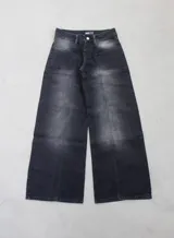 Pantalón de denim rígido negro, tiro alto, de corte ancho (wide leg) y largo. Presenta costuras visibles en el frente que simulan un diseño de paneles.