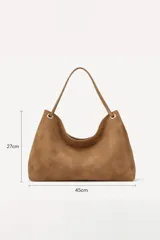 Cartera tipo hobo de gamuza color marrón oscuro, con asa única y detalles de argollas metálicas plateadas en los extremos.