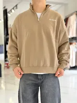 Buzo gris oscuro de corte oversize con cuello alto y cierre frontal parcial. Cuenta con mangas largas y puños elásticos, además de un pequeño bordado con texto en el pecho.