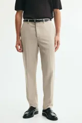 Pantalón de traje beige de corte slim fit, con cierre frontal con cremallera y corchete oculto, trabillas para cinturón, bolsillos laterales y bolsillos traseros ribeteados. Cuenta con raya marcada al frente.