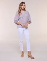 Blusa de gasa de color lila con calce holgado, cuello a la base con escote en V y cartera de botones a tono. Cuenta con fruncidos en el cuello y hombros que otorgan volumen, manga tres cuartos estilo abullonado con puño elastizado y ruedo suavemente redondeado.