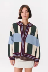 Cardigan oversize de punto con diseño de bloques de color en tonos blanco, verde oscuro y celeste, cuello redondo y cierre frontal con botones. Cuenta con ribetes acanalados a rayas en burdeos y celeste en la botonadura, cuello, puños y dobladillo.