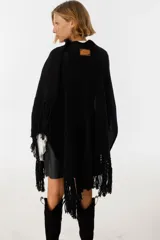 Ruana negra de tejido de punto con flecos y aplique de cuero vacuno con manchas blancas.