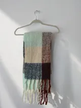 Bufanda amplia y abrigada con diseño de cuadros en tonos gris, beige, marrón y azul, terminada con flecos en los extremos.