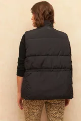 Chaleco puffer color crudo, sin mangas, con cuello alto, cierre frontal con cremallera, bolsillos frontales con solapa y cordón ajustable en la cintura.
