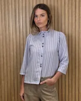 Camisa de algodón color blanco, con cuello alto con volados, mangas tres cuartos con detalles de bordado ingles y cierre frontal con botones de nácar.