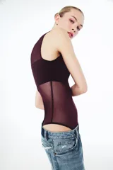 Body sin mangas de cuello redondo, confeccionado en una combinación de tul transparente y paneles de tela opaca a tono. Presenta un diseño ajustado con cierre inferior mediante botones a presión.