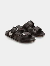 Sandalias de cuero marrón chocolate, con dos tiras anchas en el empeine provistas de grandes hebillas y detalles metálicos plateados en estilo western.