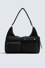 Bolso de hombro negro, fabricado en tejido técnico, con múltiples bolsillos exteriores, incluyendo uno con cierre de cremallera y otro lateral. El compartimento principal y un bolsillo interior también tienen cierre de cremallera. Cuenta con un asa de hombro ajustable.
