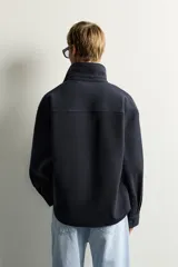 Sobrecamisa de ajuste relajado en color azul marino, con cuello de solapa, manga larga con puño abotonado y cierre frontal con botones. Presenta bordados contrastantes en el frente con la inscripción "St. Louis Worldwide Goods" en tonos naranja y blanco.