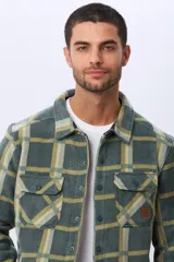 Sobrecamisa leñadora de polar a cuadros en tonos verde militar, beige y azul claro. Cuenta con dos bolsillos frontales con solapa, dos bolsillos laterales y cierre con botones a presión. Interior de micropolar.