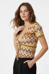 Top de punto con estampado de zigzag multicolor, cuello en V y cierre frontal con lazo anudado. Presenta mangas cortas y un ajuste al cuerpo.