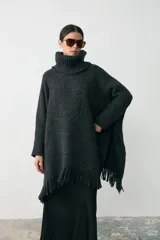 Poncho de tejido artesanal en color negro, con cuello alto tipo polera, mangas largas y terminación con flecos en el ruedo. Presenta una etiqueta de cuero decorativa en la parte inferior.
