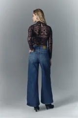 Jean de corte oxford confeccionado en denim azul con lavado desgastado y bigotes. Presenta tiro alto, pierna ancha que se ensancha desde la cadera hacia el ruedo, cierre frontal con botón y pequeñas roturas decorativas.