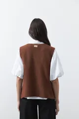 Chaleco tejido color marrón con bordados artesanales de motivos florales y geométricos en color crema. Presenta cuello redondo, cierre frontal con botones y diseño sin mangas.