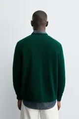 Cárdigan de punto en color verde oscuro, con cuello en pico, manga larga y cierre frontal con botones. Presenta acabados en rib en puños y bajo.