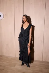 Vestido largo negro con volados verticales, tajo delantero, escote en V y finos tirantes cruzados en la espalda.