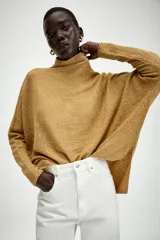 Jersey de punto con textura, color crudo, de cuello subido y manga larga. Presenta un diseño holgado con bajo asimétrico y aberturas laterales.