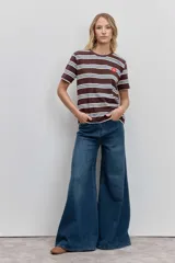 Remera de manga corta con cuello redondo, confeccionada en tejido de punto con diseño de rayas horizontales en tonos marrón, blanco y celeste. Presenta un pequeño parche circular rojo en el pecho.