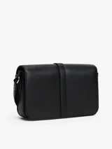 Cartera de hombro negra con solapa frontal y correa ajustable. Presenta un broche metálico dorado con el monograma TH en el centro.