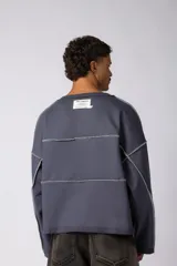 Buzo oversize de corte boxy, confeccionado en algodón rústico de alto gramaje en color beige. Presenta cuello redondo con borde crudo, mangas largas y una estampa frontal con el texto VCP delimitado por líneas horizontales blancas.