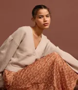 Cardigan corto de punto color beige claro, con escote en V, manga larga abullonada y cierre frontal de botones. Posee bolsillos delanteros tipo parche.